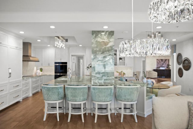 kitchen with a spacious island, tasteful backsplash, black appliances, wall chimney range hood, and white cabinets