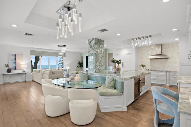 kitchen featuring tasteful backsplash, white cabinetry, exhaust hood, and light stone counters