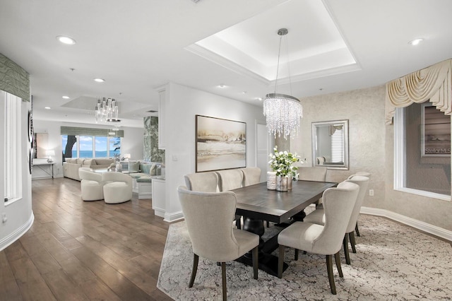 dining room with an inviting chandelier, a tray ceiling, and dark wood-type flooring