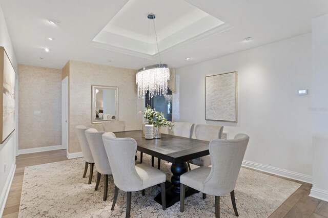 dining space with baseboards, a raised ceiling, an inviting chandelier, and light wood-style flooring