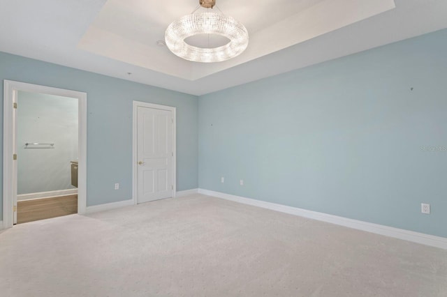 unfurnished bedroom featuring ensuite bathroom, carpet, a raised ceiling, and baseboards