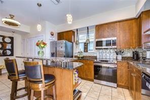 kitchen with a kitchen island, stainless steel appliances, a kitchen breakfast bar, kitchen peninsula, and light tile patterned floors