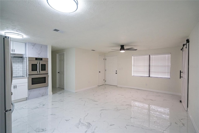 unfurnished living room with ceiling fan, a barn door, and a textured ceiling