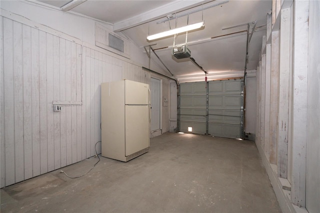 garage featuring white refrigerator, wooden walls, and a garage door opener