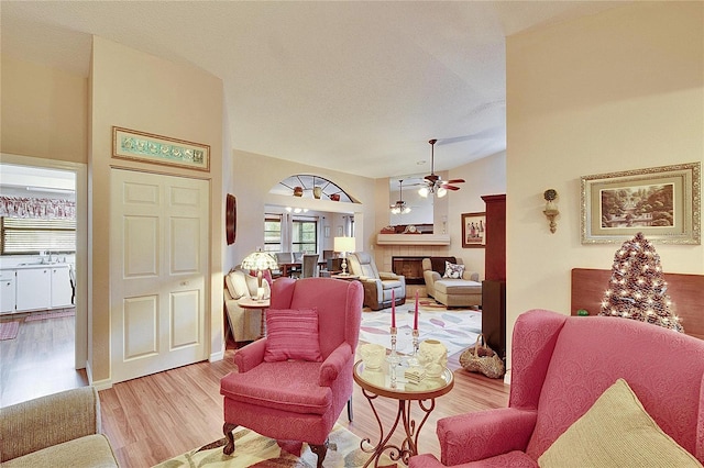 living room with sink, vaulted ceiling, a tile fireplace, ceiling fan, and light hardwood / wood-style floors