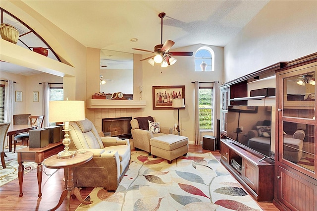 living room featuring a tile fireplace, lofted ceiling, ceiling fan, and light hardwood / wood-style floors