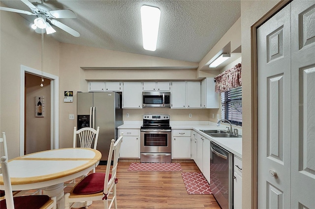 kitchen with sink, white cabinetry, vaulted ceiling, light hardwood / wood-style flooring, and stainless steel appliances