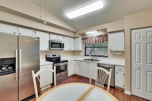 kitchen with dark wood-type flooring, sink, white cabinetry, vaulted ceiling, and appliances with stainless steel finishes