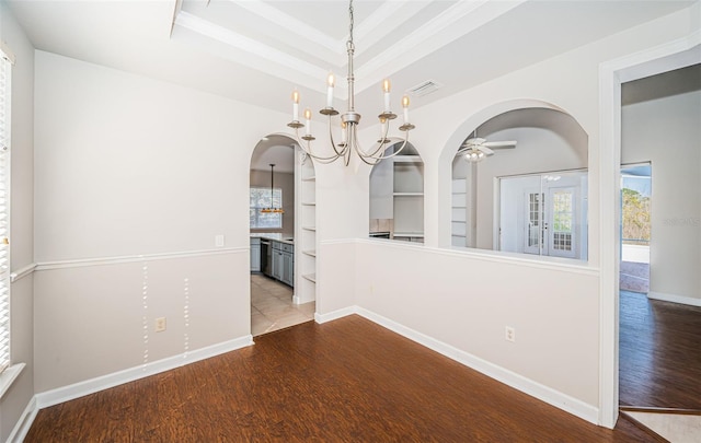 unfurnished dining area with hardwood / wood-style flooring, a tray ceiling, built in features, and a notable chandelier