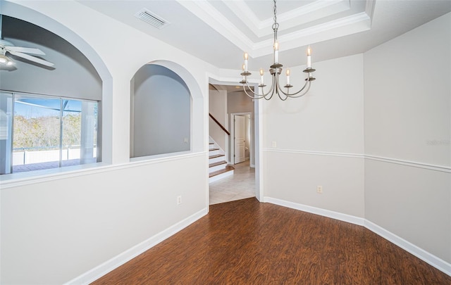 unfurnished dining area featuring a raised ceiling, ornamental molding, ceiling fan with notable chandelier, and dark hardwood / wood-style flooring