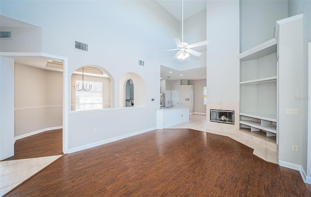 unfurnished living room featuring built in features, ceiling fan with notable chandelier, a fireplace, and light hardwood / wood-style floors