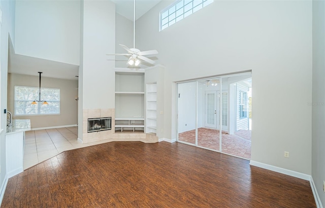 unfurnished living room with a tile fireplace, built in features, ceiling fan, and light wood-type flooring