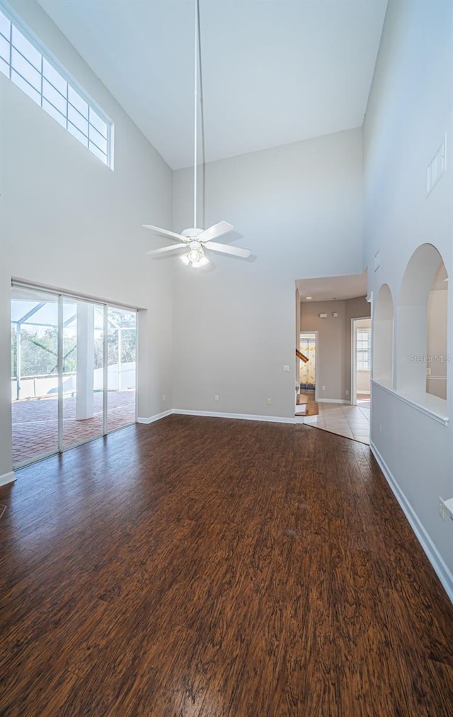 unfurnished living room featuring dark wood-type flooring, ceiling fan, and a high ceiling