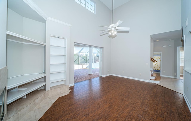 unfurnished living room featuring a towering ceiling, hardwood / wood-style floors, ceiling fan, and built in shelves