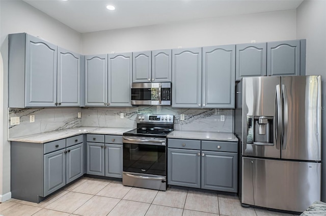 kitchen with tasteful backsplash, appliances with stainless steel finishes, gray cabinets, and light tile patterned flooring