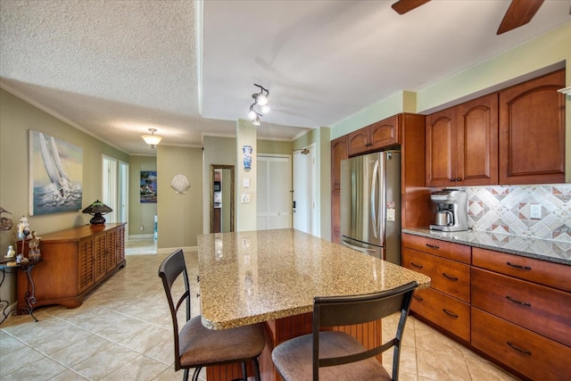 kitchen with crown molding, a textured ceiling, stainless steel refrigerator, backsplash, and light stone counters