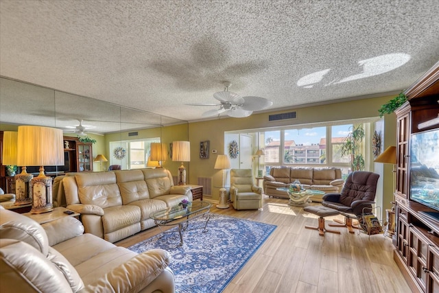 living room with a textured ceiling, light hardwood / wood-style flooring, and ceiling fan