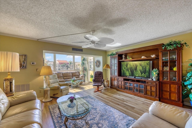 living room with light wood-type flooring, a textured ceiling, ceiling fan, and ornamental molding