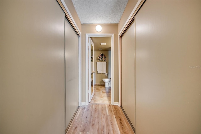 hallway with light wood-type flooring and a textured ceiling