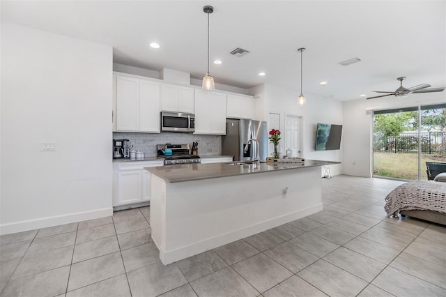 kitchen with white cabinets, appliances with stainless steel finishes, decorative light fixtures, sink, and a kitchen island with sink