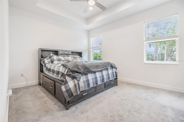 bedroom with ceiling fan, a tray ceiling, and light carpet