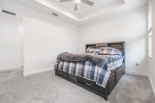 carpeted bedroom with ceiling fan and a raised ceiling