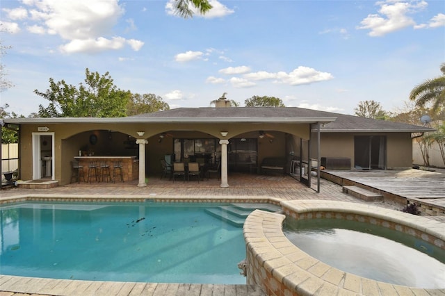 view of swimming pool with a wooden deck, exterior bar, an in ground hot tub, and ceiling fan