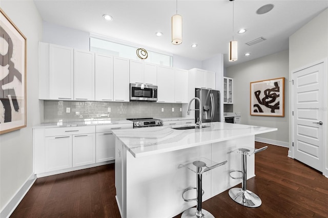 kitchen with pendant lighting, white cabinets, appliances with stainless steel finishes, and a center island with sink