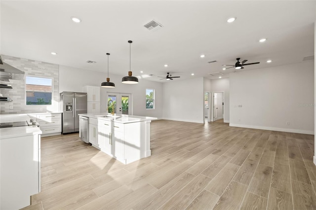 kitchen with pendant lighting, white cabinetry, stainless steel appliances, french doors, and an island with sink