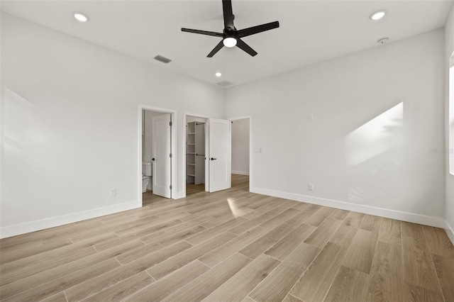 unfurnished bedroom with ceiling fan, light hardwood / wood-style floors, connected bathroom, and a walk in closet