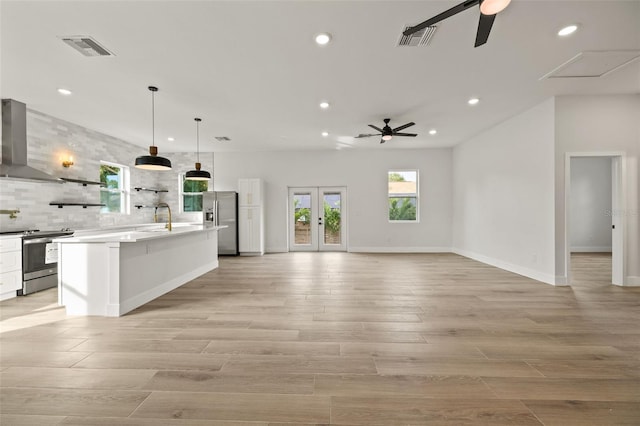 kitchen featuring white cabinetry, wall chimney range hood, decorative light fixtures, french doors, and stainless steel appliances