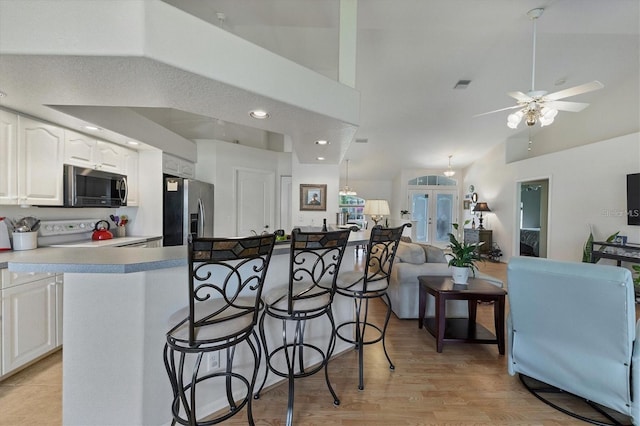 kitchen with a breakfast bar area, stainless steel appliances, light hardwood / wood-style floors, white cabinets, and vaulted ceiling