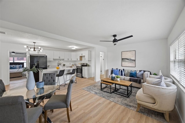 living room with ceiling fan with notable chandelier and light hardwood / wood-style flooring