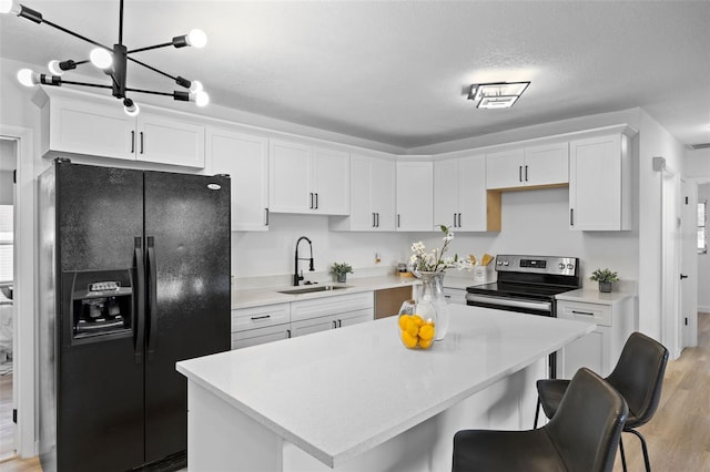 kitchen with white cabinets, light hardwood / wood-style floors, sink, black fridge, and stainless steel range with electric stovetop