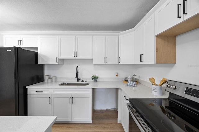 kitchen with a textured ceiling, white cabinets, stainless steel range with electric cooktop, black refrigerator, and sink