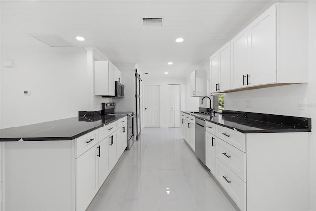 kitchen with kitchen peninsula, sink, white cabinetry, a barn door, and stainless steel appliances