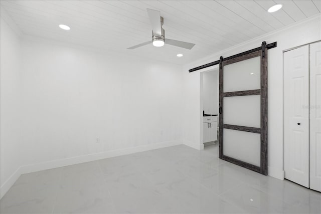 empty room featuring ceiling fan, a barn door, and crown molding