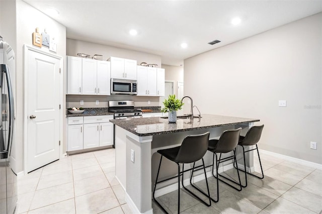 kitchen featuring sink, white cabinetry, appliances with stainless steel finishes, dark stone counters, and a kitchen island with sink