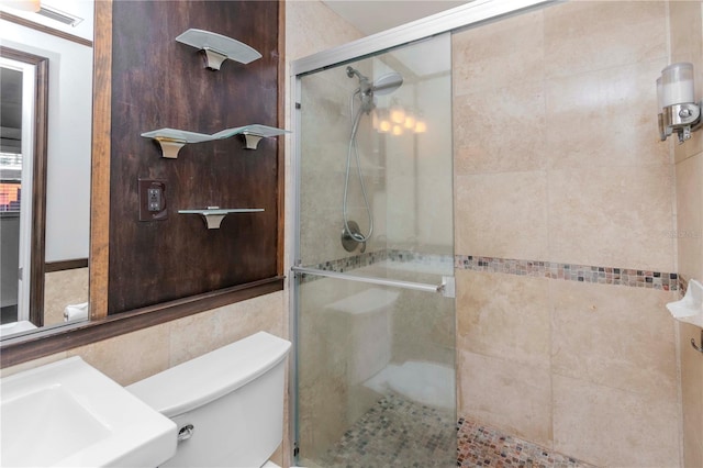 bathroom featuring a shower with door, toilet, and tile walls