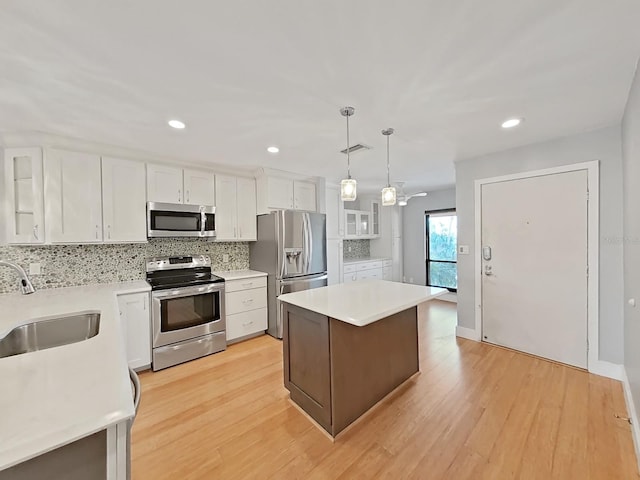 kitchen featuring sink, hanging light fixtures, stainless steel appliances, white cabinets, and a kitchen island