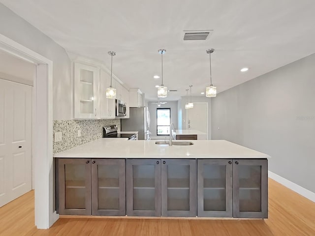 kitchen featuring sink, appliances with stainless steel finishes, white cabinetry, decorative backsplash, and decorative light fixtures