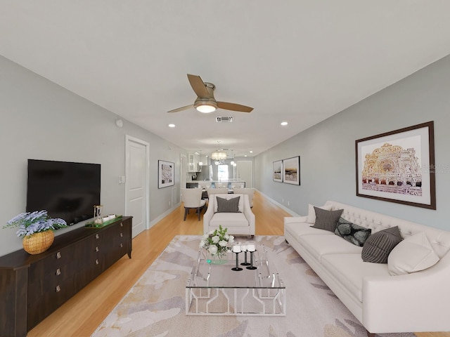 living room featuring ceiling fan with notable chandelier and light wood-type flooring