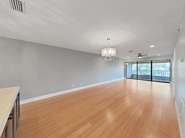 unfurnished living room with ceiling fan with notable chandelier and light hardwood / wood-style flooring