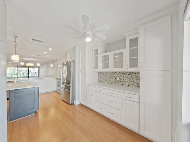 kitchen with appliances with stainless steel finishes, decorative light fixtures, white cabinetry, backsplash, and light wood-type flooring