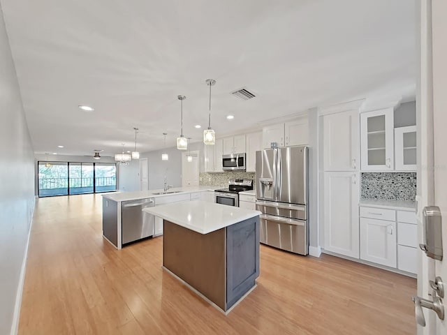 kitchen featuring a kitchen island, appliances with stainless steel finishes, decorative light fixtures, white cabinetry, and kitchen peninsula