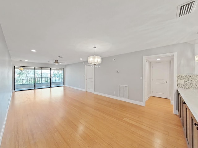 unfurnished living room with ceiling fan with notable chandelier and light hardwood / wood-style floors