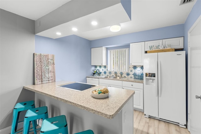 kitchen featuring white cabinetry, sink, a breakfast bar area, and white fridge with ice dispenser