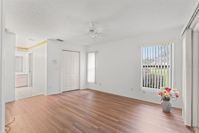 unfurnished room featuring ceiling fan, a textured ceiling, light hardwood / wood-style flooring, and a healthy amount of sunlight