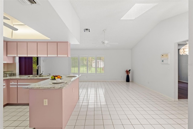 kitchen featuring light tile patterned floors, vaulted ceiling with skylight, sink, a kitchen island, and ceiling fan