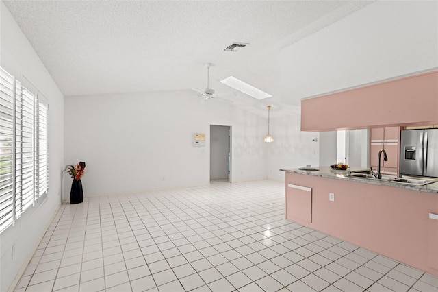 kitchen with stainless steel refrigerator with ice dispenser, lofted ceiling with skylight, sink, light tile patterned floors, and a wealth of natural light